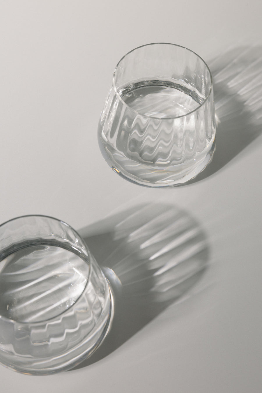 Two clear glass tumblers with water on a light gray background