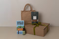 Gift set with a book, body oil, roasted nuts, and box on a neutral background