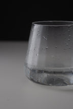 A close-up of a clear glass tumbler with condensation droplets, set against a dark black background and a light gray surface.