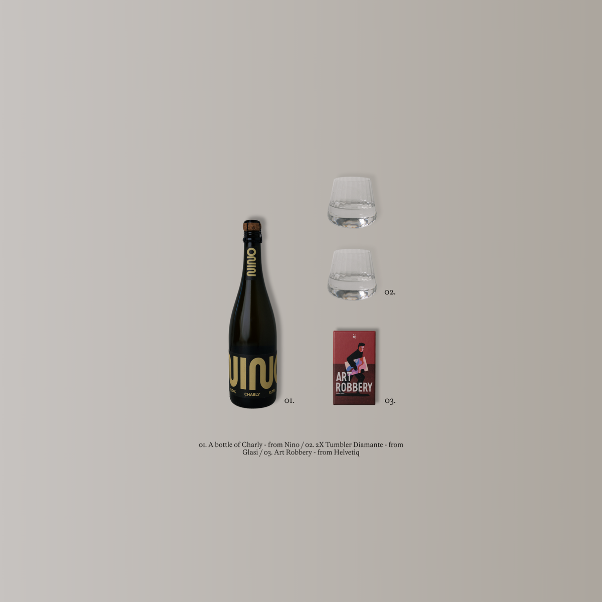 A minimalist product layout on a light warm-gray background featuring a dark bottle with gold lettering, two small clear glasses, a small red book or card, and tiny text labels. The bottle appears to be the main product, with the other objects acting as styled props.