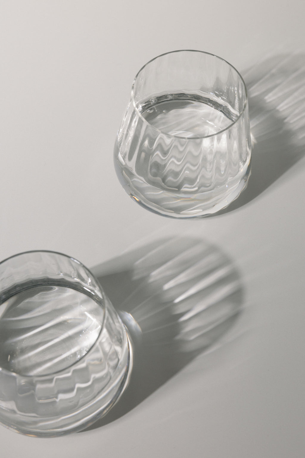 Two clear glass tumblers with water on a light gray background