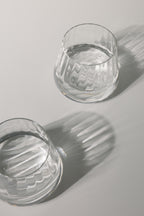 Two clear glass tumblers with water on a light gray background