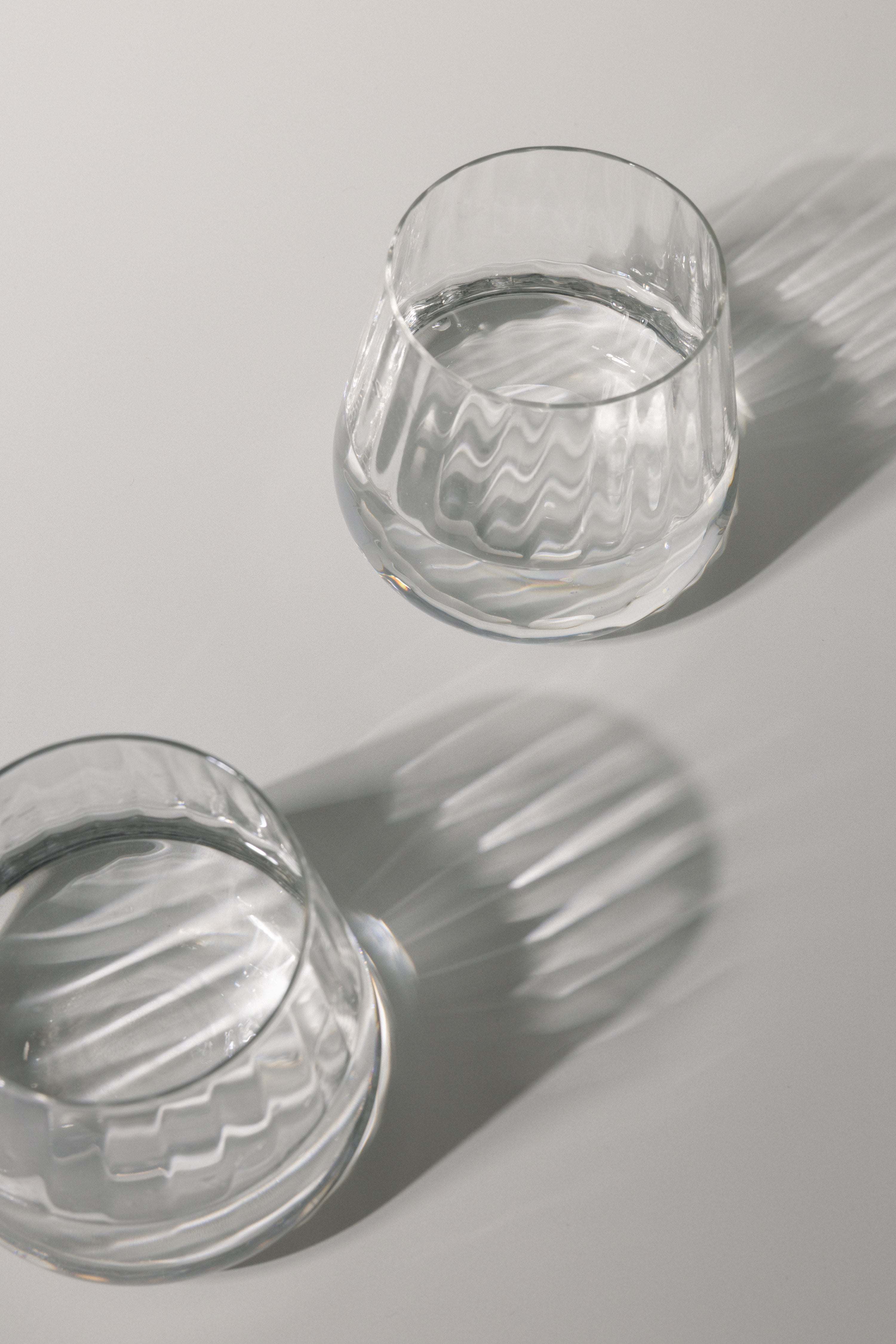 Two clear glass tumblers with water on a light gray background