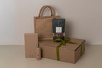 Brown paper bag, box, and bottle with a green ribbon on a beige background