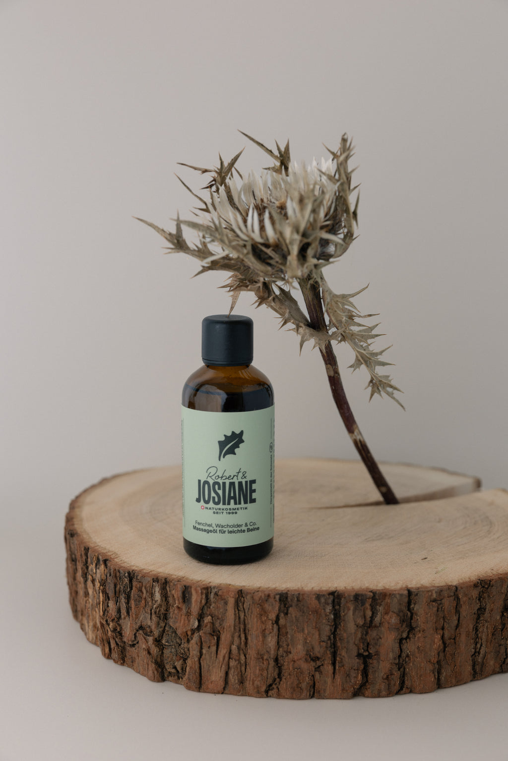 Bottle of boidy oil Robert & Josiane on a wooden platform with a dried plant