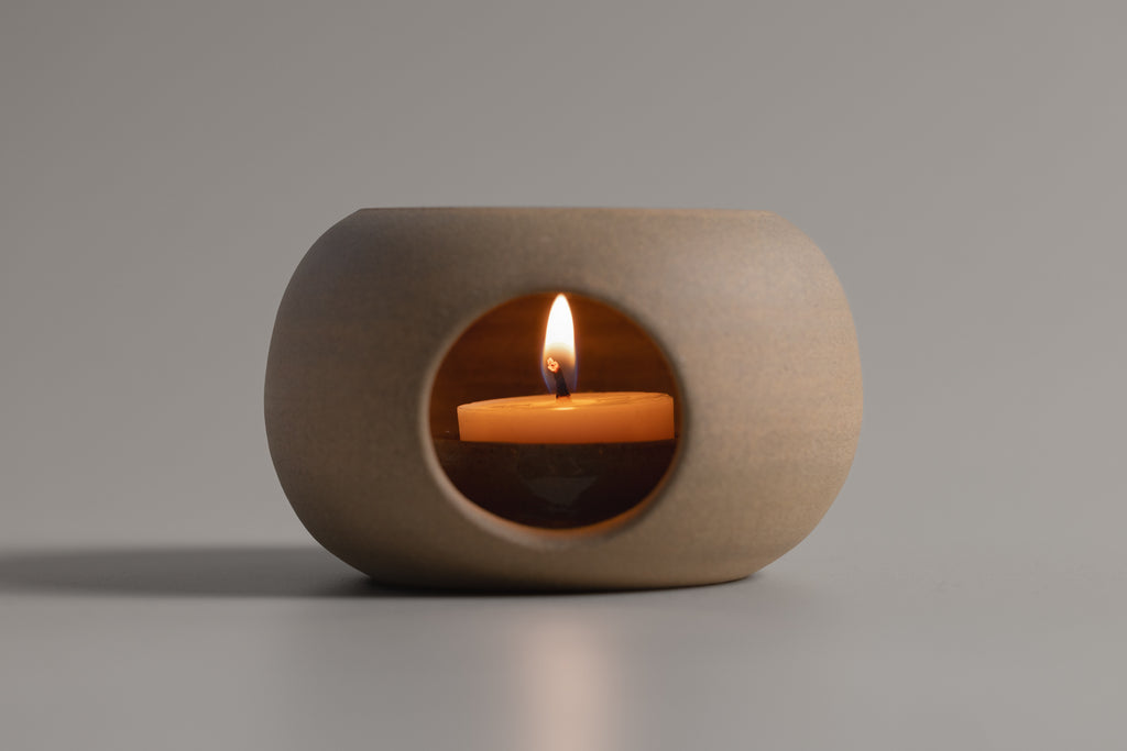 Ceramic candle holder with a lit candle on a gray background