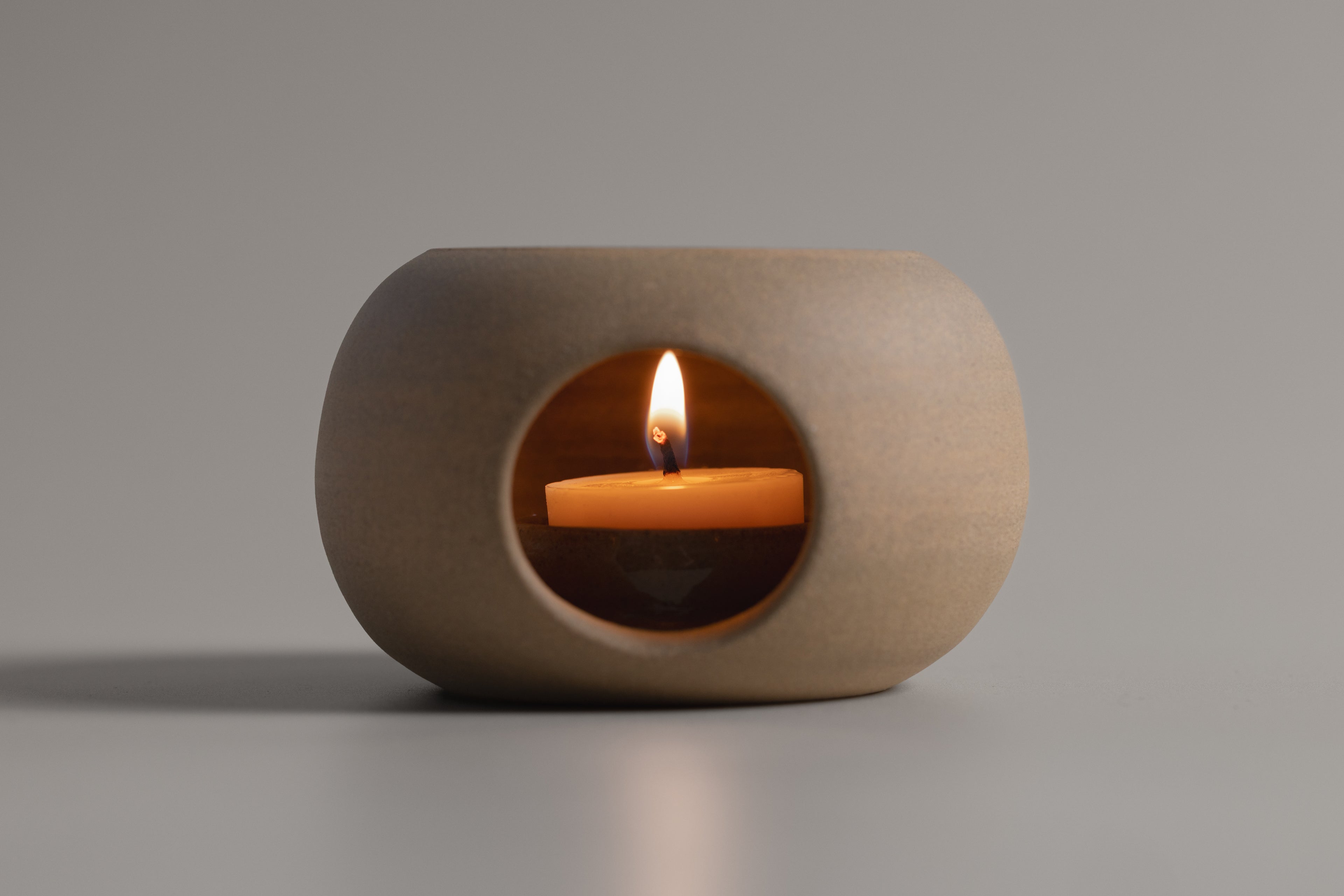 Ceramic candle holder with a lit candle on a gray background