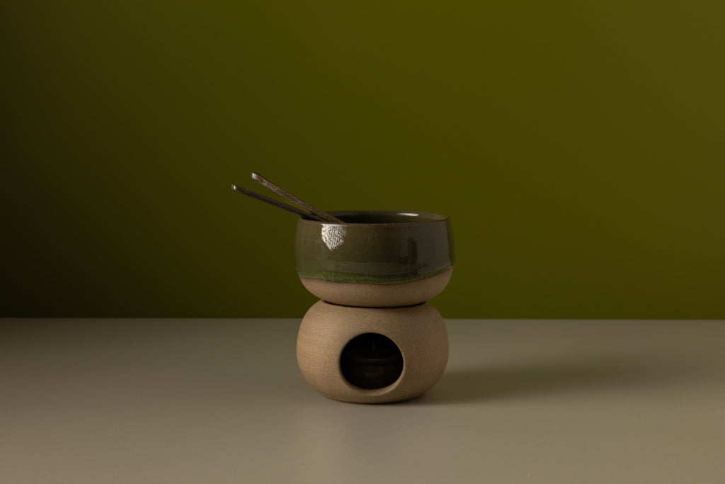 Ceramic hot chocolate set with bowl and spoon on a wooden base against a green background