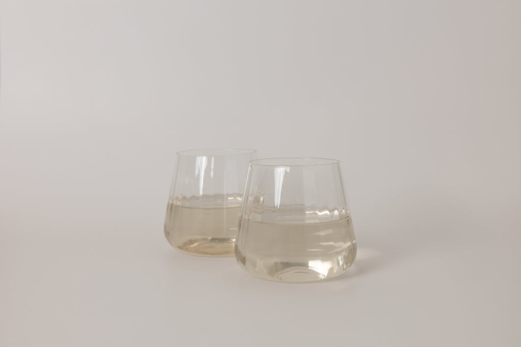 Two clear glass tumblers filled with a light liquid on a white background