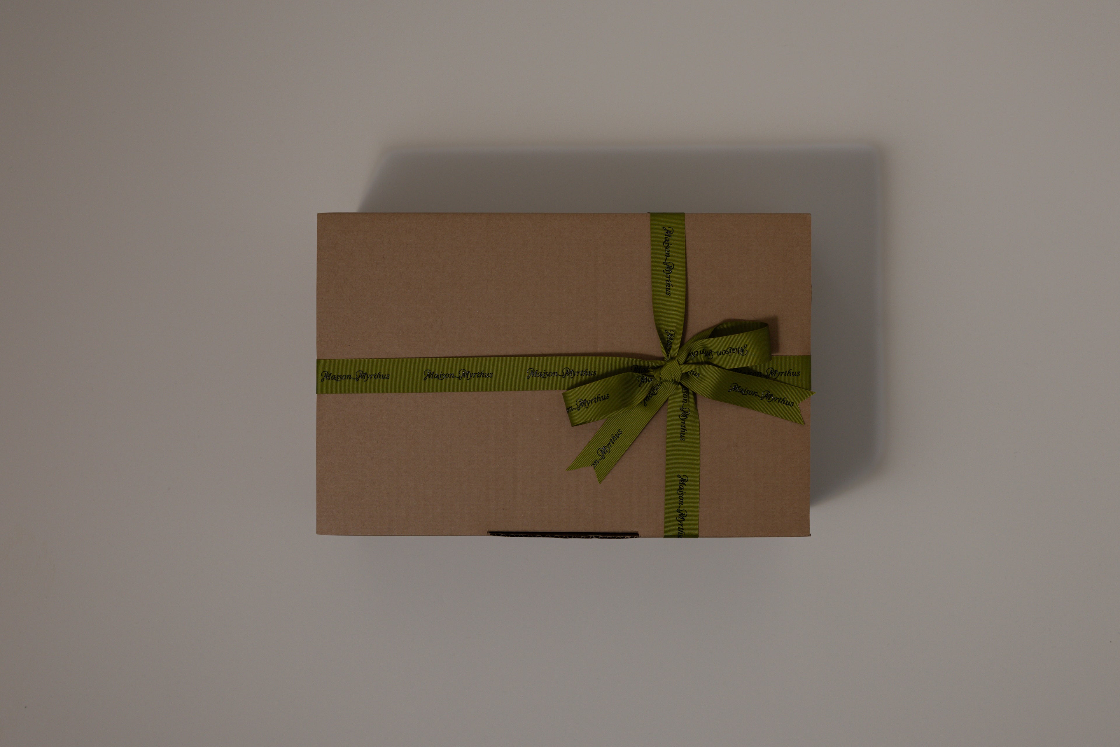 Brown gift box with a green ribbon on a light gray background