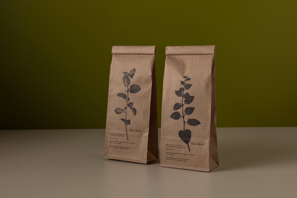 Two brown paper bags with leaf designs on a green background. herbal tea made in switzerland.