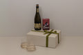 Alcool free bottle of wine, gift box with a green ribbon, board game and two glasses on a white surface.