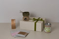 Gift box with a candle holder, cermaic cup, fondue set, laflor chocolate, hot cocoa, and chocolate hazelnut dragee, and wood box with signature maison myrthus ribbon on a neutral background