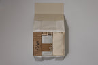 Box containing muslin blanket, laflor chocolate, herbal tea and baby rattle with a visible brand name on a plain background