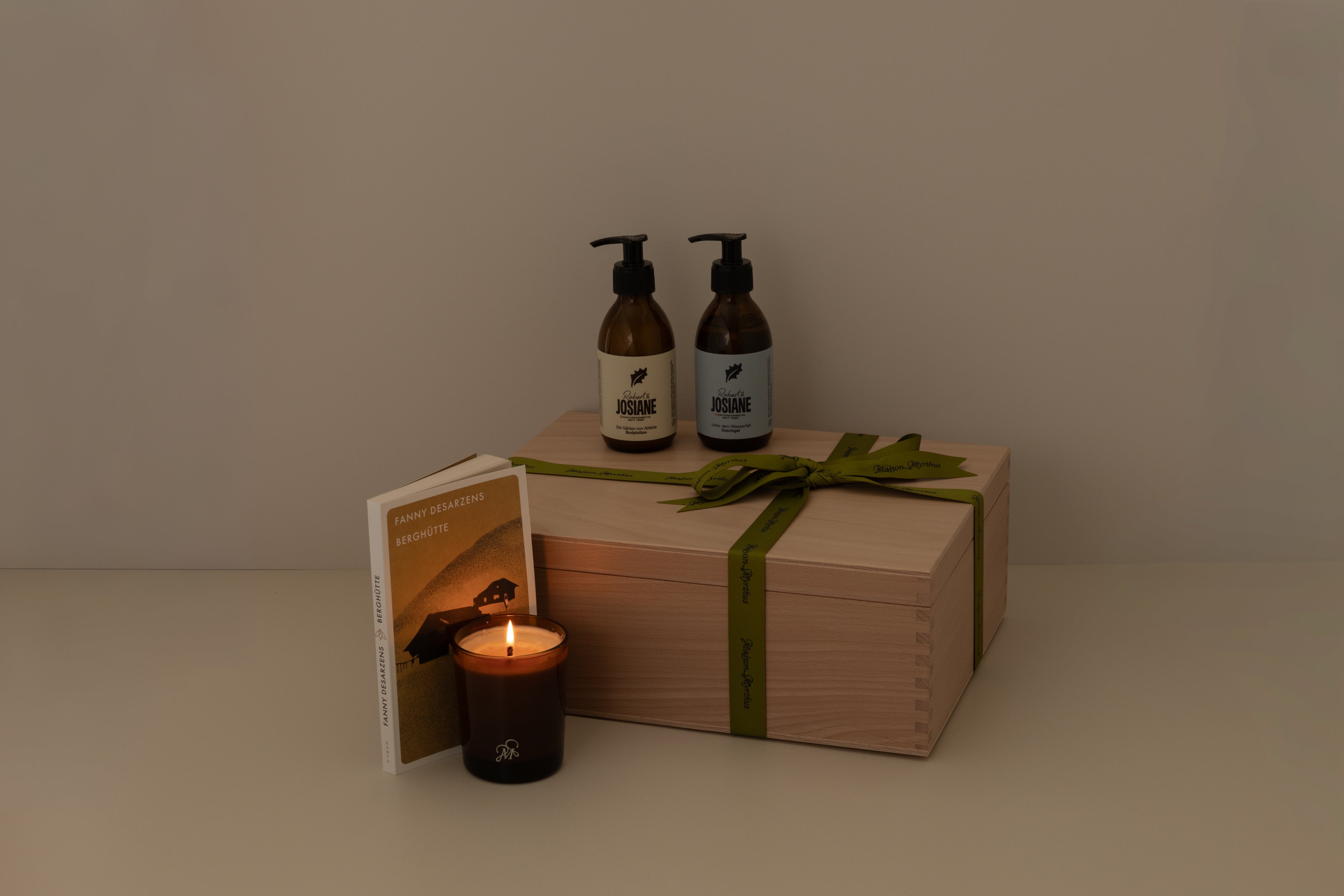 Gift box with two bottles of body lotion and shower gel, a candle, a book and a wood box on a neutral background